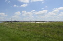 A large warehouse like facility sits behind fields of wild grass and weeds.