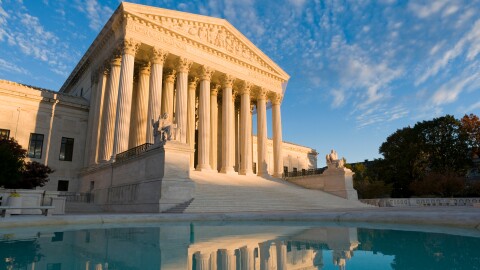The front of the US Supreme Court in Washington, DC, at dusk. The building is reflected in the ornamental pool.