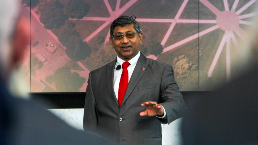 A man in a suit and tie with an OSU pin speaks on a stage. 