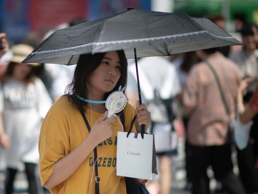 A woman uses a portable fan to cool herself in Tokyo on Tuesday as Japan suffers from a heat wave. Scientists say extreme weather events will likely happen more often as the planet gets warmer.