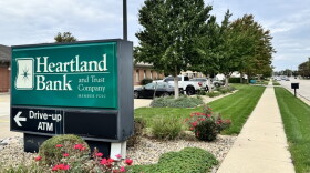 A Heartland Bank and Trust sign directs customers toward the ATM in front of a row of trees.