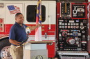A man gestures to a fire truck while standing at a lecturn.
