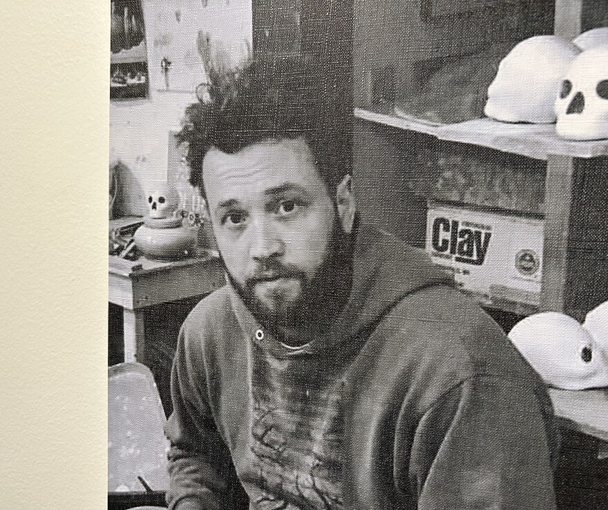 A man wearing a sweatshirt with a beard in front of ceramic pieces.