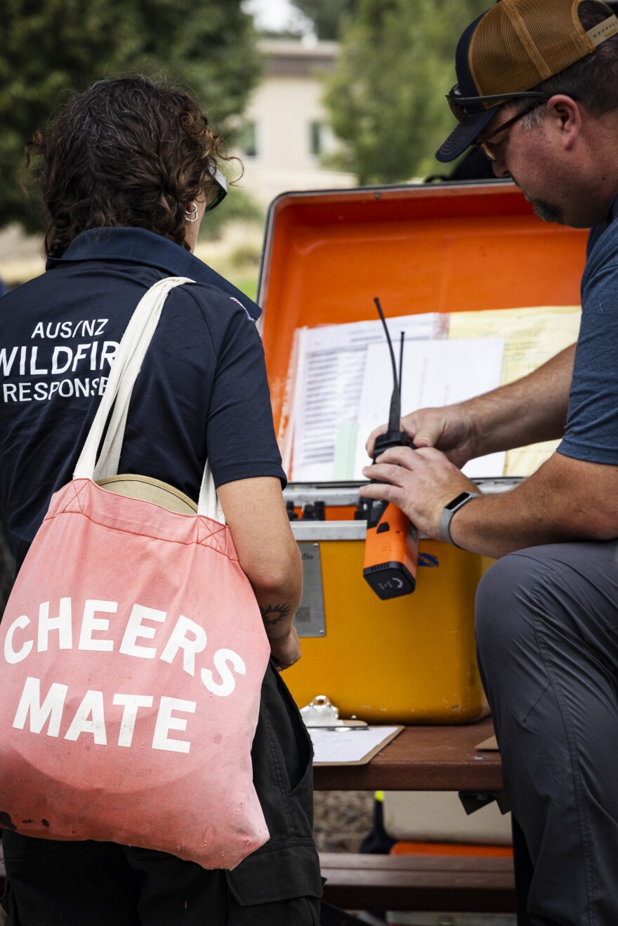 A firefighter with a "Cheers Mate" tote bag gets the radio they'll be using on the fireline.