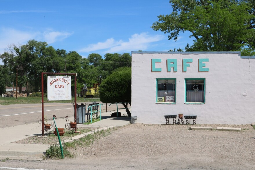 Sugar City, once a thriving sugar manufacturing center, features a sign next to a shuttered café.