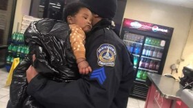 A police officer holds an infant boy with a coat wrapped around him in a pizza shop.