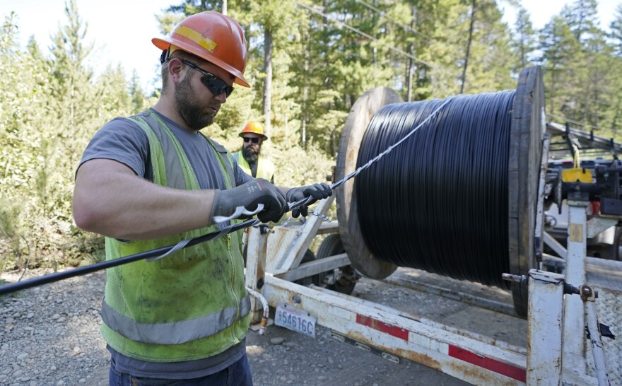 Skylar Core, right, a worker with the Mason County (Wash.) Public Utility District, installs a hanger onto fiber optic cable as it comes off of a spool, Wednesday, Aug. 4, 2021, while working with a team to install broadband internet service to homes in a rural area surrounding Lake Christine near Belfair, Wash. High-speed broadband internet service is one of the key areas of President Joe Biden's $1 trillion bipartisan infrastructure package being considered by lawmakers in Washington, DC. (AP Photo/Ted S. Warren)