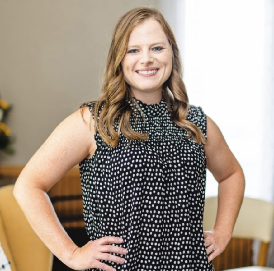 A woman stands in an office with her hands on her hips.