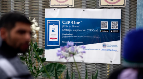 People waiting to apply for asylum stand in front of a sign for the CBP One app as they camp near the pedestrian entrance to the San Isidro Port of Entry, linking Tijuana, Mexico with San Diego.