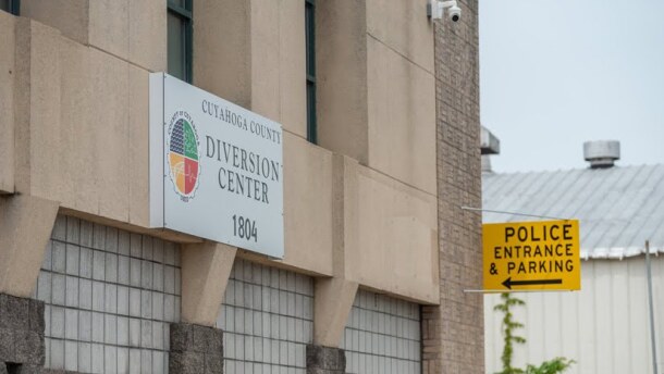 A white sign on a brick and concrete building announces Cuyahoga County's diversion center. Beside it, another sign points to parking for police.