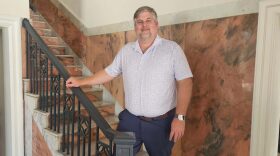 Man with grey hair wears polo shirt and stands next to staircase 