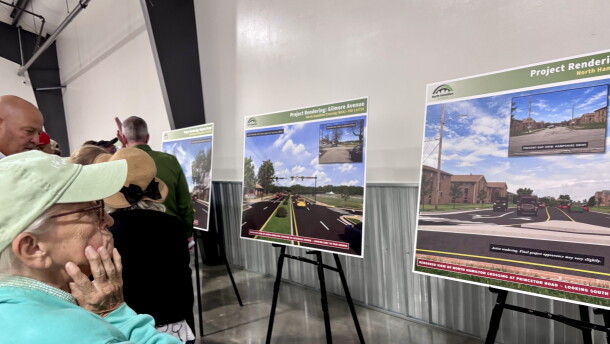 A woman in a blue sweatshirt looks at a sign displaying a rendering of a road with cars on it.