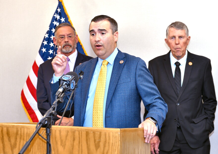Man in blue suit and yellow tie stands at podium speaking 