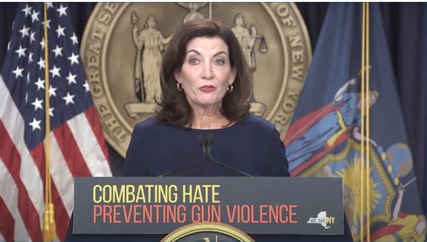 Gov. Kathy Hochul stands at a podium that says, "COMBATING HATE PREVENTING GUN VIOLENCE," in front of the state seal and between a U.S. and state flag.