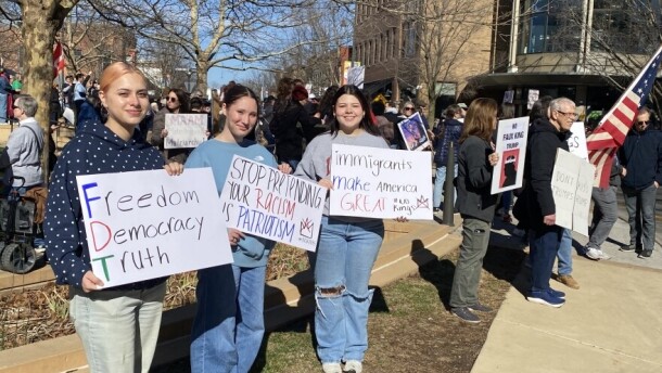 Three young women hold protest signs in Uptown Normal