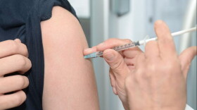 health worker sticks syringe into arm of a person with rolled up black sleeve