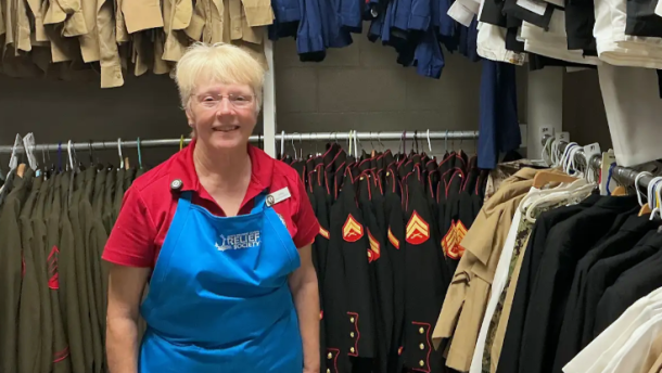 Navy-Marine Corps Relief Society volunteer Audrey Faragher stands among racks of military uniforms at the organization’s thrift shop on NAS Pensacola. Faragher, who has volunteered at the shop since 2024, helps sort, price and organize donated items for military families.