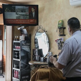 A barber cuts the hair of a customer as they watch the news on television following the announcement that Israel and Hamas have agreed to the first phase of a peace plan to pause the fighting, in Jerusalem, Thursday, Oct. 9, 2025.
