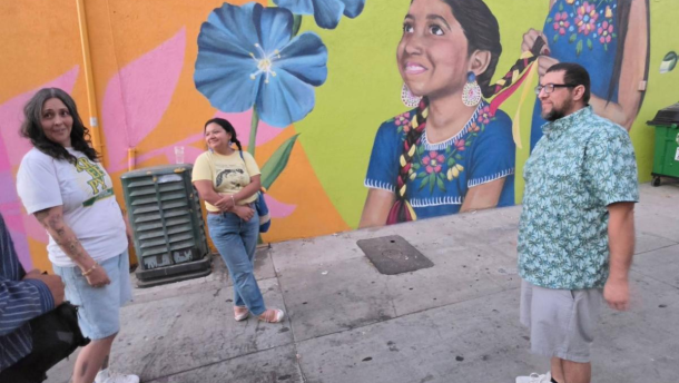 Photo of folks standing against a painted mural of an Indigenous child.