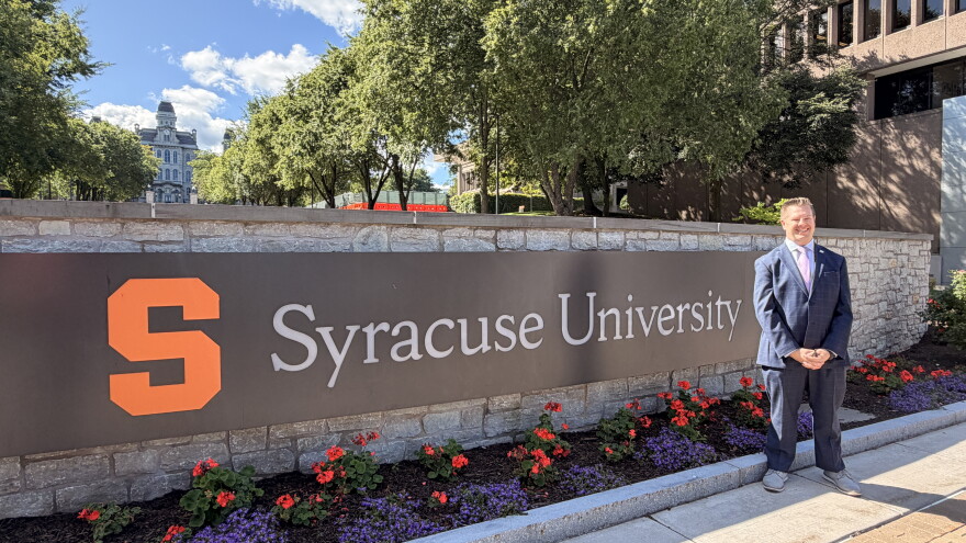 Syracuse City Auditor Alex Marion stands in front of a Syracuse University sign
