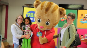 Visitors pose with Daniel Tiger in front of colorful hanging tiles.
