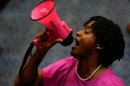 Glack woman in a pink dress and wearing pearls speaks into a pink megaphone