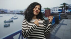Woman holds passport and hand on chest on street promenade by the seaside near small boats