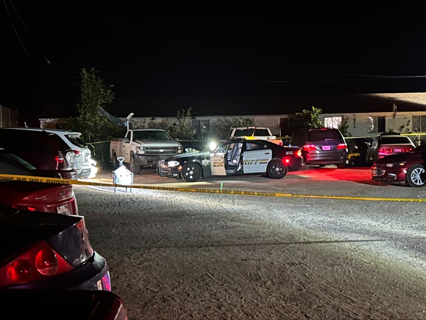 A Sheriff's car in a gravel parking lot surrounded by other cars and yellow caution tape.