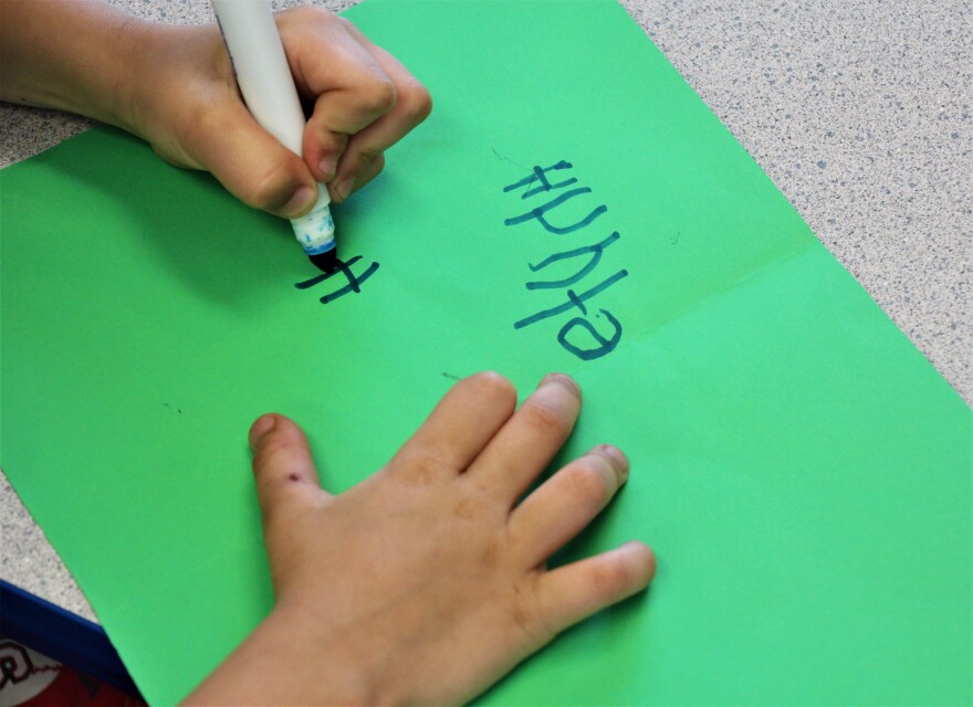 A child's hands writing with marker on a piece of construction paper.