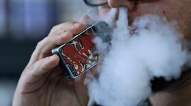FILE - In this Friday, Oct. 4, 2019 file photo, a man using an electronic cigarette exhales in Mayfield Heights, Ohio. A judge has cleared the way for Montana to temporarily ban the sale of flavored e-cigarettes and other flavored vaping products. State officials say they plan to implement the ban Wednesday, Dec. 18, 2019.