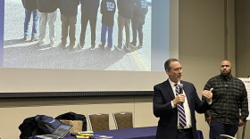Two men stand in a room and projected behind them is an image of DEA officers. 