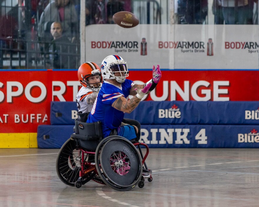 Matt Daniels, in a blue jersey and a sports wheelchair, extends his arms to catch a football. 