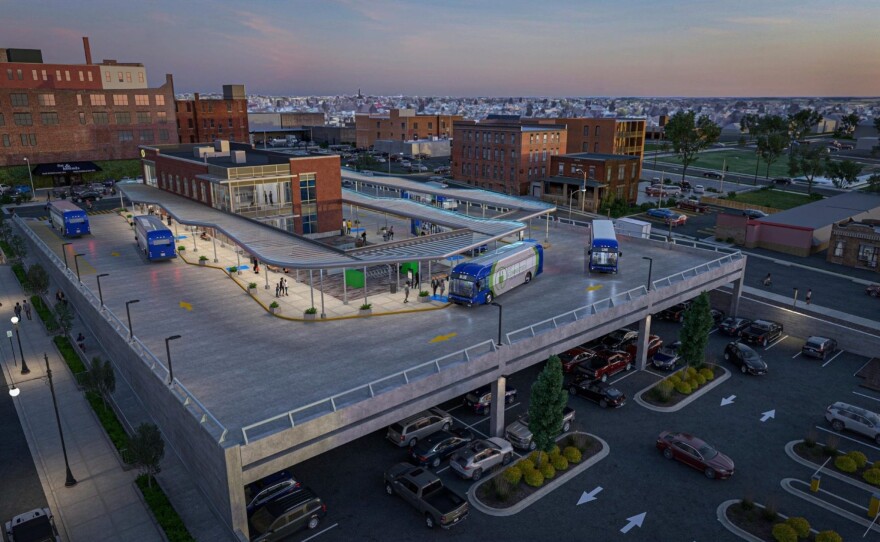 A computer design of the new facility in an aerial view with several buses and cars parked around the area.