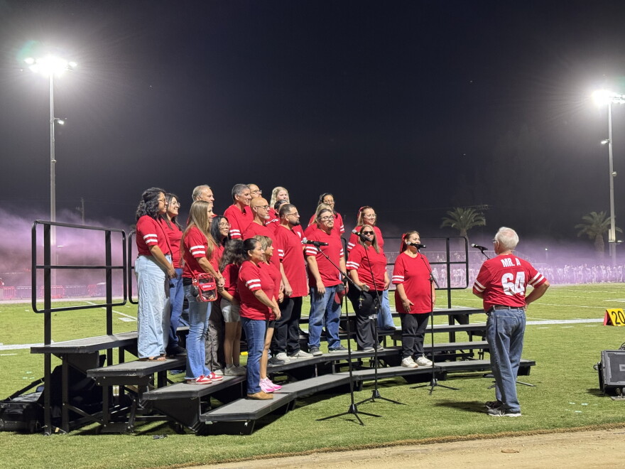 Community members sing the national anthem during the Kerman High School football homecoming game.