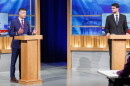 Two men in suits stand at podiums in a TV studio