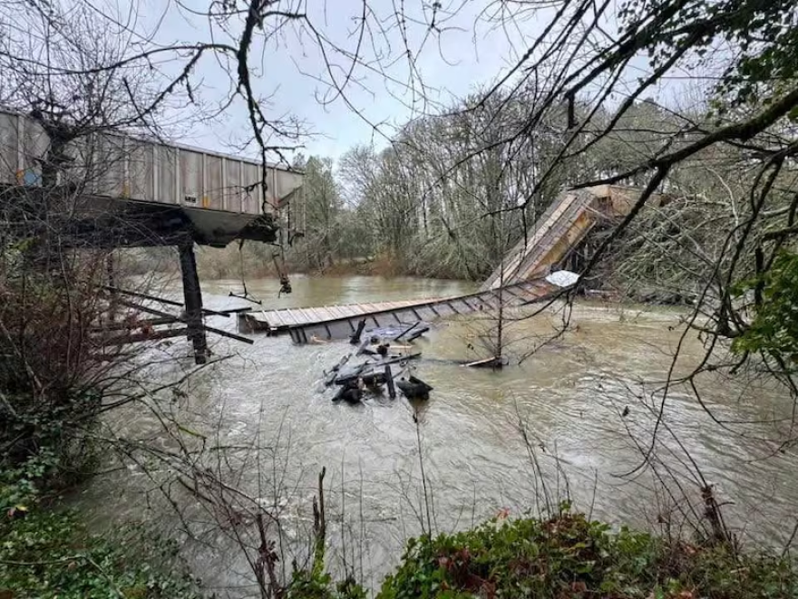 A collapsed train trestle and train cars in a river.