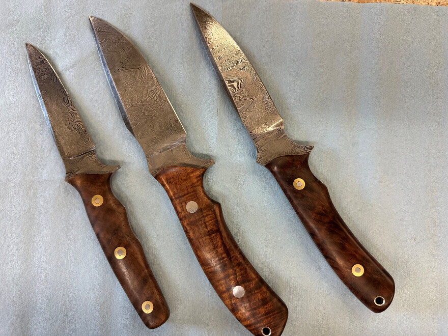 Three knives with brown wooden handles on a gray paper.