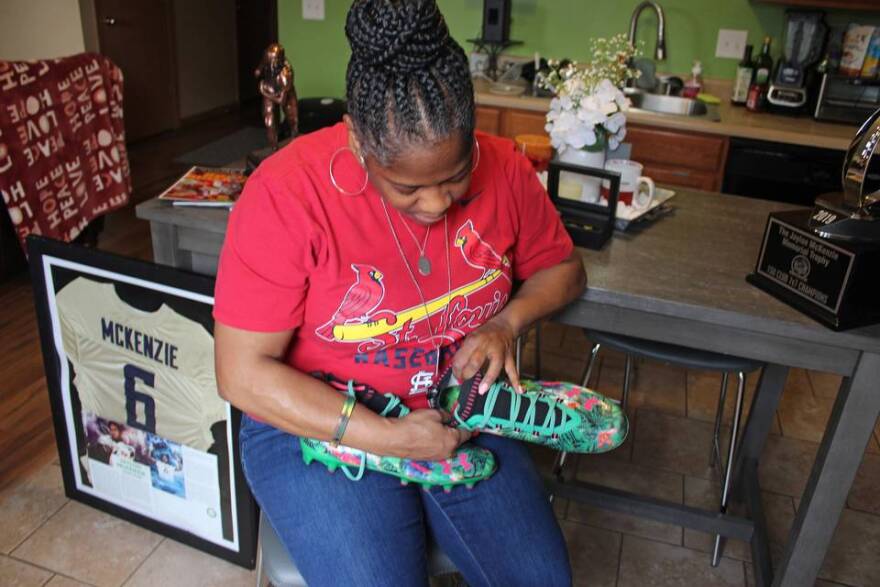 Sukeena Gunner holds a pair of green football cleats that belonged to her son, Jaylon McKenzie. 