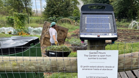A sign posted to a fence announces the community garden hours in four languages.