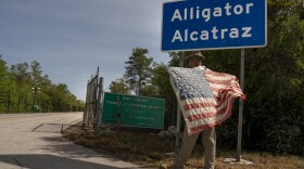 A man holds an American flag in front of the entrance to Alligator Alcatraz, a new immigrant detention center located at the Dade-Collier Training and Transition Airport in Ochopee, Fla., July 12, 2025. Florida raced to open the Everglades detention center on July 3, eager to help President Trump’s immigration crackdown by providing more detention capacity. (Ava Pellor/The New York Times)