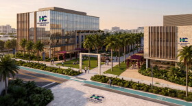 Artist rendering shows two mid-size buildings, with a wide walkway lined by palm trees between them. Both have the signage HC Hillsborough College. The building on the left is mostly glass. People are seen on the wide sidewalk walkway and adjoining sidewalks. Green area cross the front of the image by the adjoining sidewalk. 
