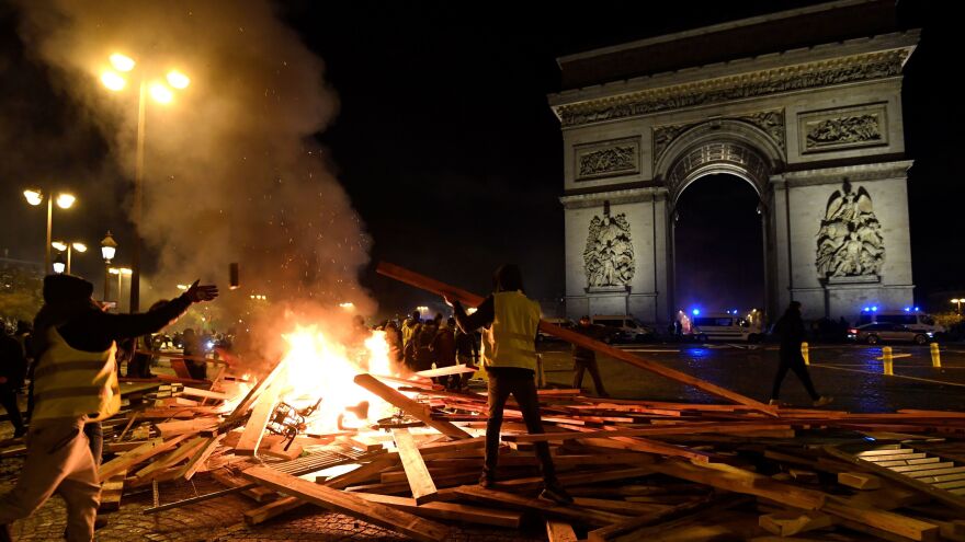 A yellow vest protestor adds to a fire near The Arc de Triomphe in Paris on Saturday, during a rally against a gas tax that will go into effect in January.