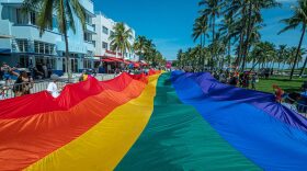 A huge multi-colored flag flies over Ocean Drive as people participate in the Pride Parade, during the Miami Beach Pride Festival, in Lummus Park, South Beach, Florida.