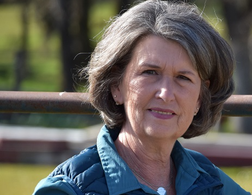 A woman with salt-and-pepper hair looks directly into the camera, smiling slightly.