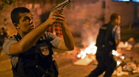 An officer from Brazilian Police Special Forces took aim Tuesday during the violent protest that broke out in one of Rio de Janeiro's slums. People there blame police for a young man's death, and say authorities are clamping down too hard in advance of this June's World Cup soccer tournament and the 2016 Summer Olympics, both of which will be held in Brazil.