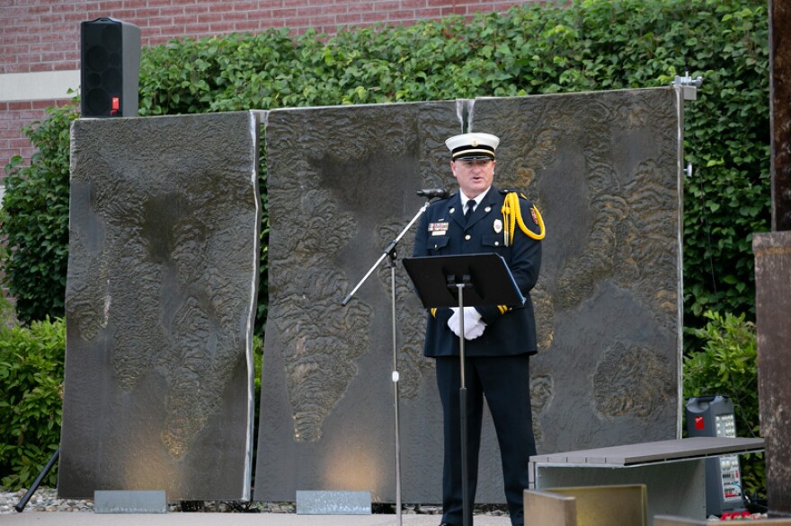 Capt. Paul Schnichels of the Overland Park Fire Department led the ceremony. Behind him is an artistic display known as “The Weeping Wall” symbolizing the nation’s tears.