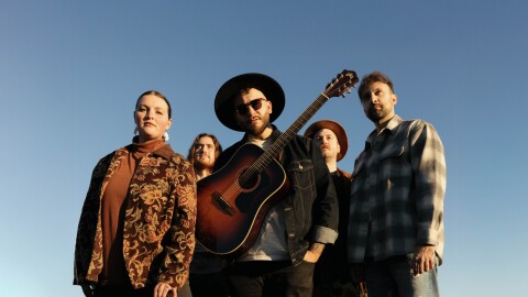 Photo of VOYAGR, with the man in the middle wearing a guitar around his body