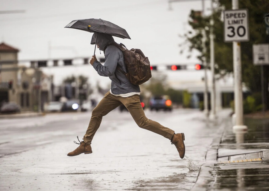 A man leaps over a large puddle on Central Avenue near the University of New Mexico on Wednesday.