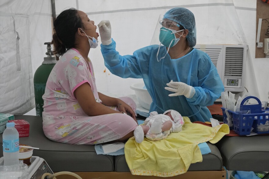 Medical Technologist Erika Alvarado performs a COVID-19 test on a patient who just delivered a baby outside a hospital in Manila, Philippines on Friday, Dec. 24, 2021. (AP Photo/Aaron Favila)