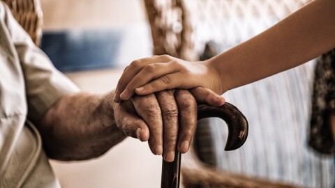 child's hand over old man's hand holding a cane.
